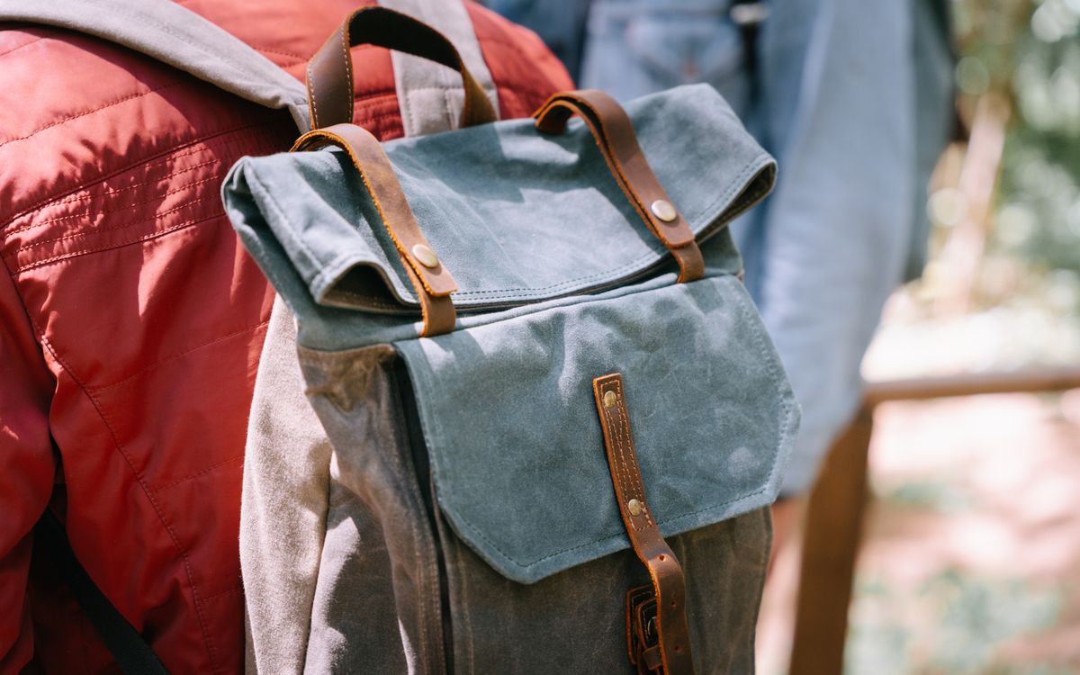 A close-up of a canvas backpack with leather straps worn on someone's back