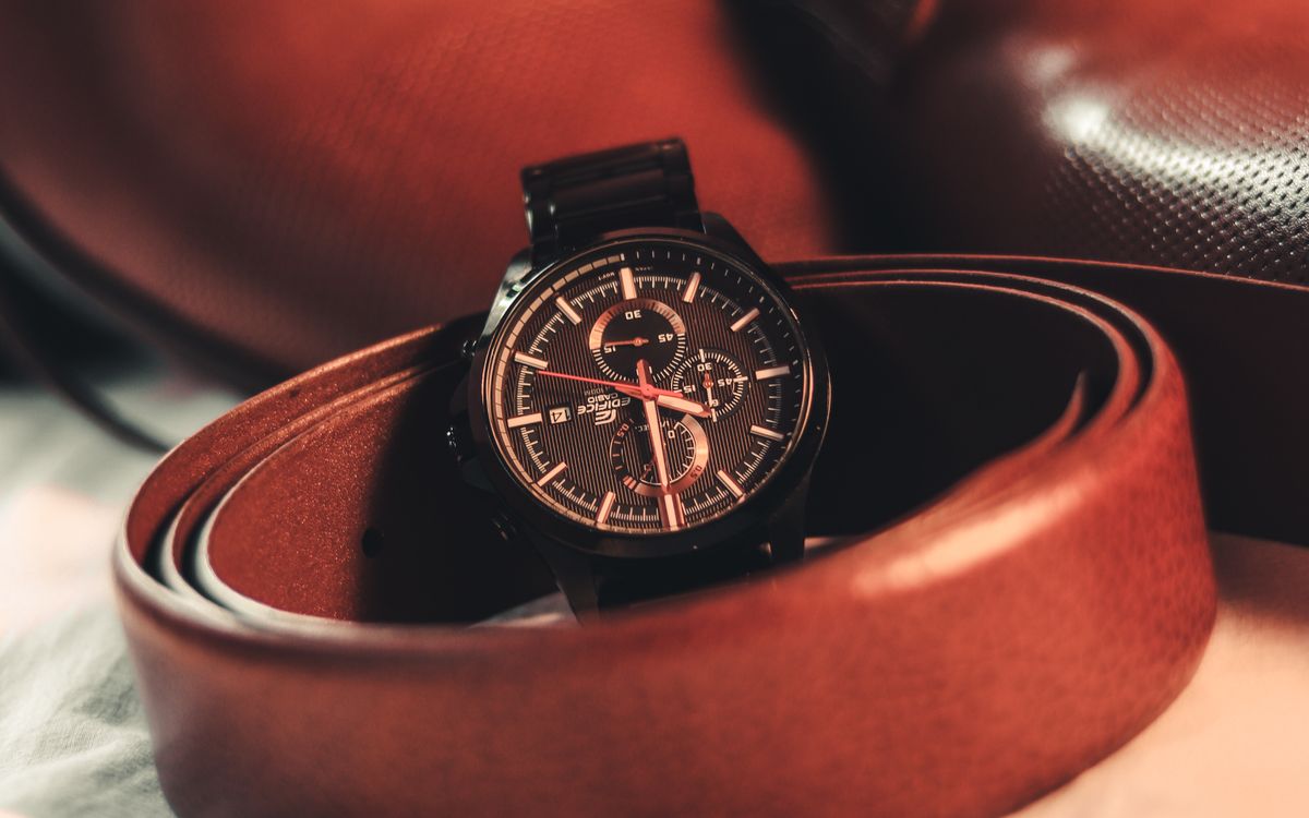 A wristwatch and a belt next to shoes