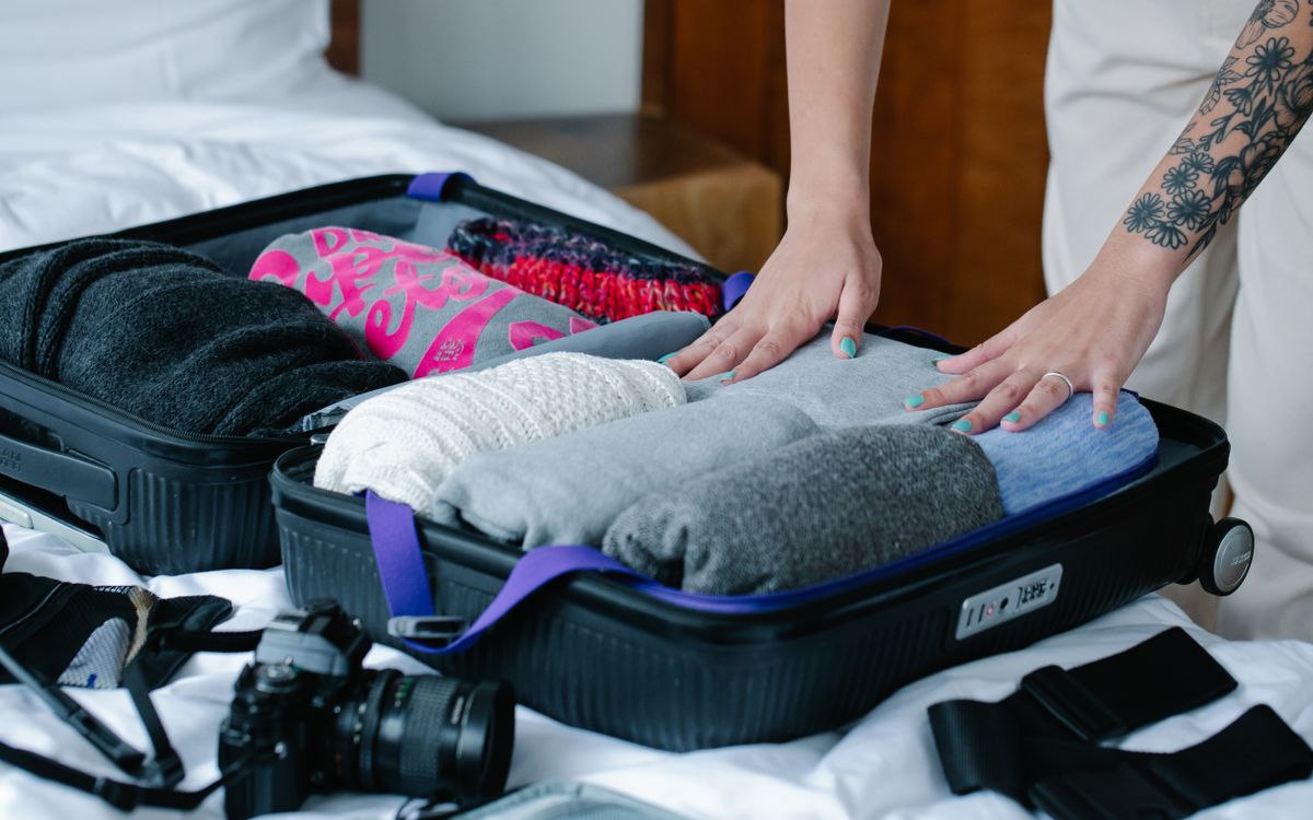 A person holding folded clothes over open luggage