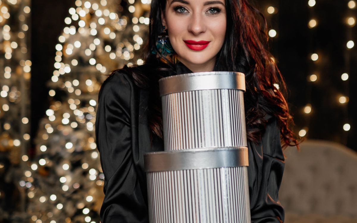 A woman holding gift boxes in front of a Christmas tree