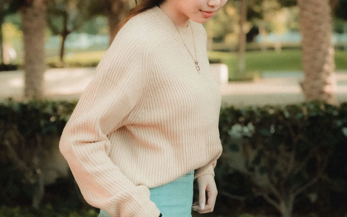 A young woman in a sweater and skirt walking through a park on an autumn morning