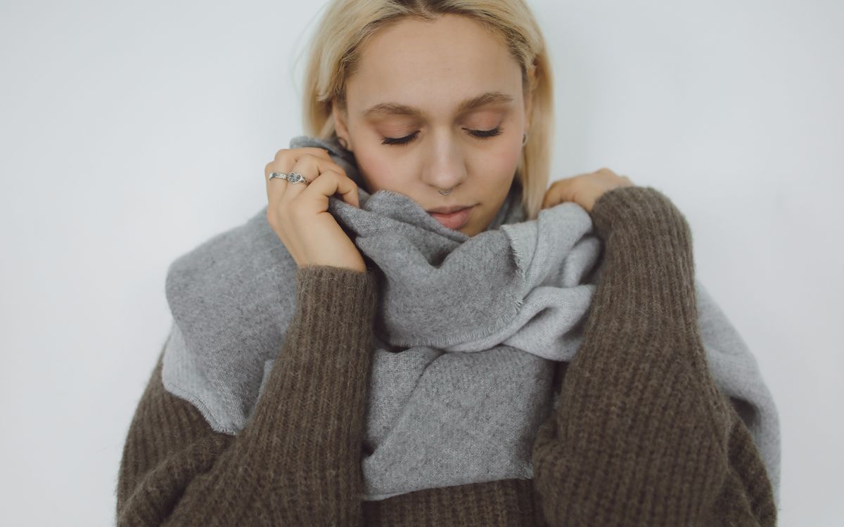 A woman in a gray sweater covering her face with a gray scarf
