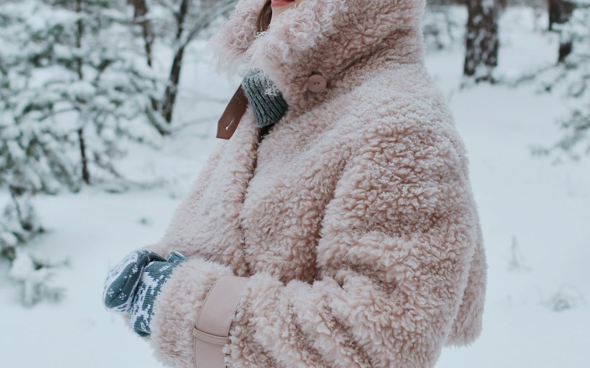 A young woman in a pink wool coat and beanie posing in a winter forest