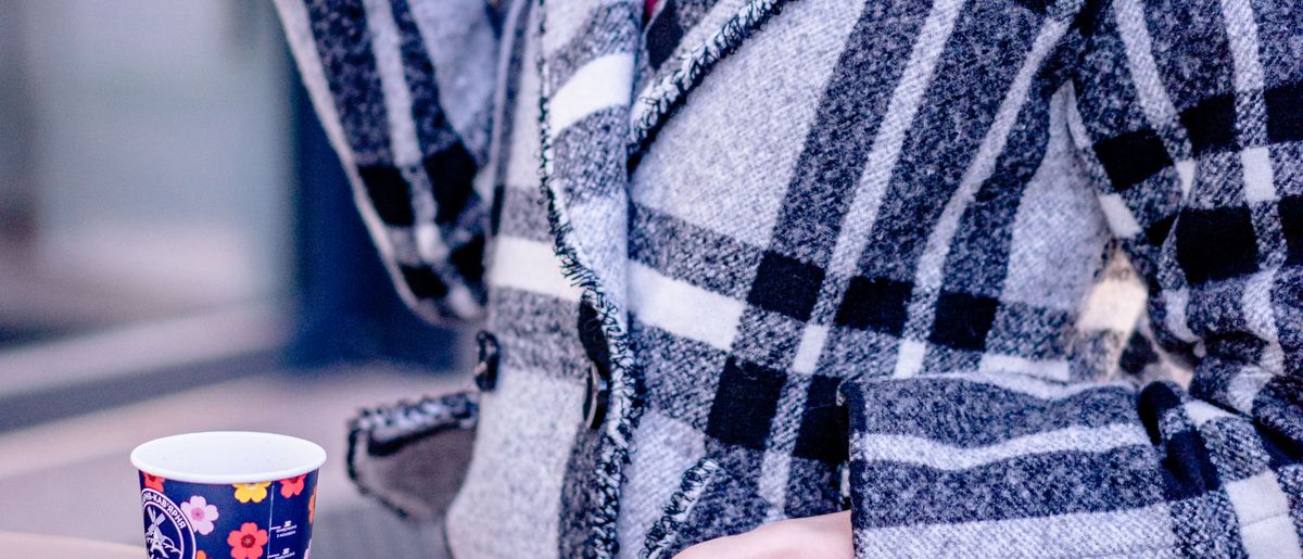 A woman in a plaid coat holding a paper cup
